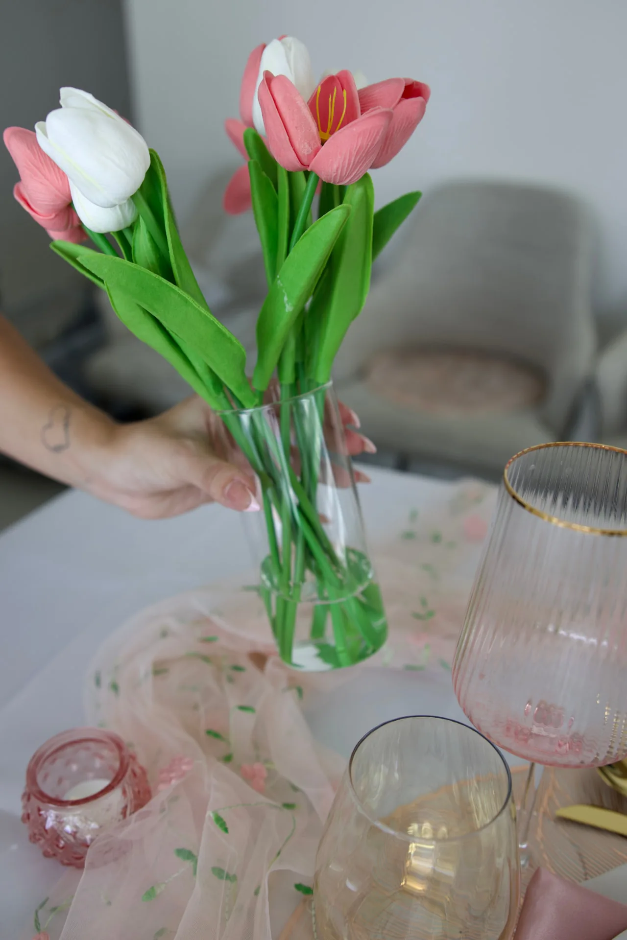 Hand placing a vase of pink and white tulips on a styled table